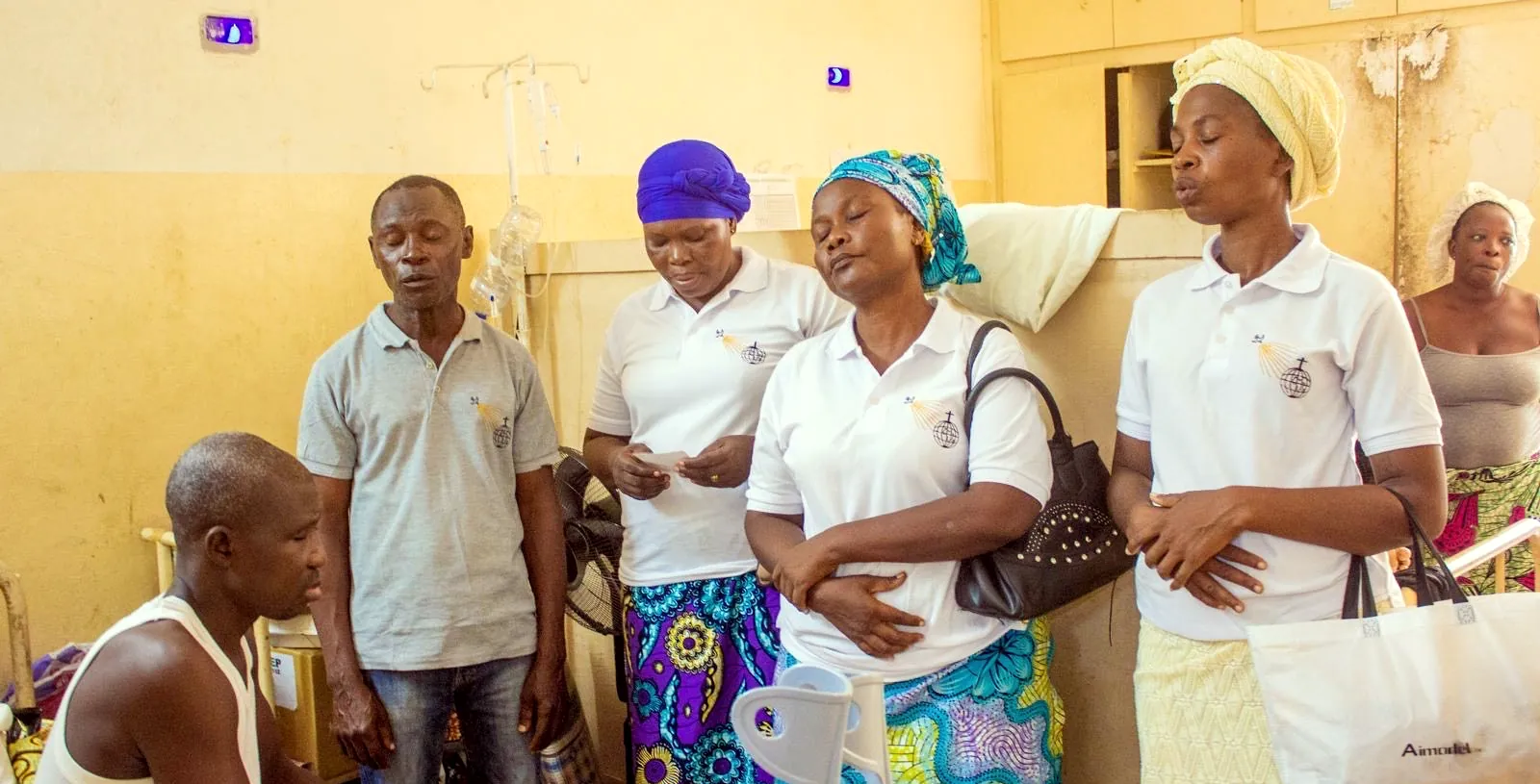 Volunteers sing and pray beside a seated patient